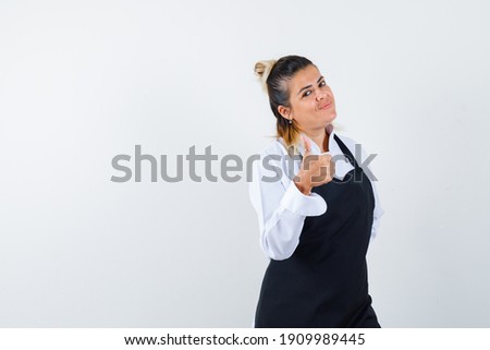  female chef showing thumb up in uniform, apron and looking happy , front view. 