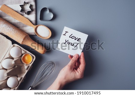 In the hands of a note I love you. Ingredients for making homemade cookies on a gray background. The concept of cooking sweets for Valentine's day, Father's Day or Mother's Day. Flat lay, top view.