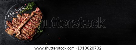 Panorama banner with Piece of cooked T-bone or aged wagyu porterhouse grilled medium rare beef steak with spices served on slate board. banner, catering menu recipe place for text, top view. Royalty-Free Stock Photo #1910020702