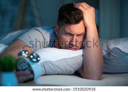 frustrated young man in bed suffering insomnia Royalty-Free Stock Photo #1910020918
