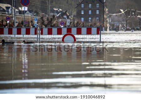 Parking lot on the Rhine flooded during high water, close-up of the barrier sign half under water with ducks in front of it.

