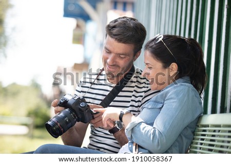 couple of tourists reviewing photos on camera sitting on bench