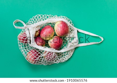 Organic apples in an opened biodegradable eco friendly string bag on green background.