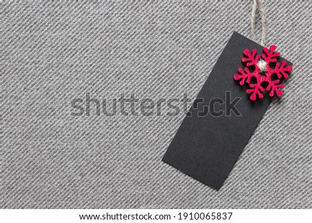 Christmas template mockup with black blank label and red wooden snowflake on textured fabric. Photo with copy blank space.