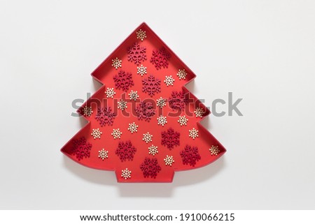 Creative Christmas greeting card with red Christmas tree outline and red white wooden snowflakes on white background.