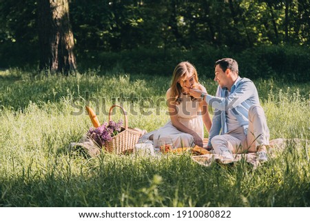 Lovely couple in love organized a picnic in the park wicker basket with flowers and food on the bedspread. happy lovers laugh and eat at the picnic. romantic date Royalty-Free Stock Photo #1910080822