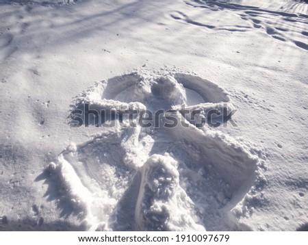 Snow angel design made in fresh, deep snow, by lying on back and moving arms up and down, and legs from side to side in winter on a sunny day