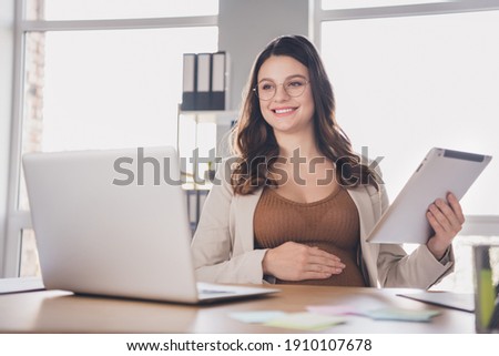 Photo portrait of pregnant woman holding tablet watching videos on laptop in modern office