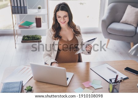 Photo portrait of pregnant lady holding laptop in one hand typing on laptop in modern office