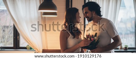 Loving couple in the evening in the living room at home. International Women's Day. A man gives a woman a bouquet of tulips on March 8. Romantic family evening at home.