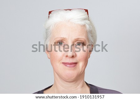 Portrait picture of a senior woman with glasses in her white hair, gray background.