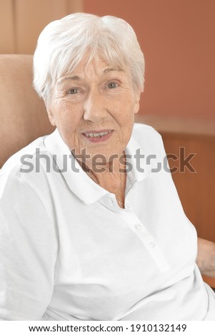 Cheerfully smiling senior woman in a comfy chair in her room at a retirement home.
