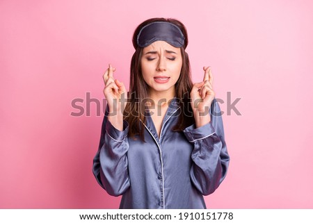 Photo portrait of hopeful girl with closed eyes fingers crossed isolated on pastel pink colored background