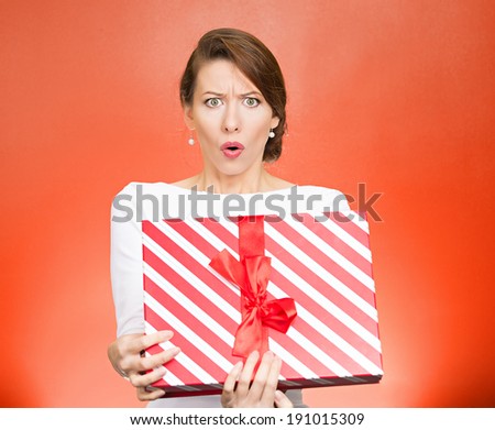 Closeup portrait young woman holding opening gift box, displeased, shocked angry, disgusted with what received, isolated red background. Negative human emotion, facial expression, feeling, reaction