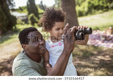 New experience. Dark-skinned cute girl holding a binocular and looking interested Royalty-Free Stock Photo #1910166457