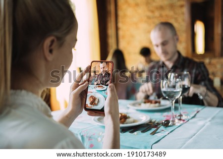 A young woman taking a photo of her partner with her smartphone in a restaurant.