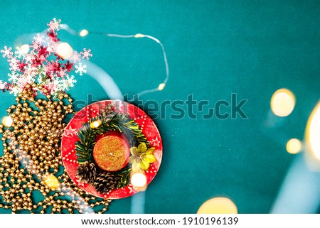 Christmas lights over a december season composition with ornaments and decorations. Top view with copy space on green background.