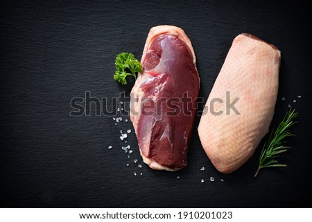Raw duck breast pieces garnished with rosemary and parsley on dark slate background