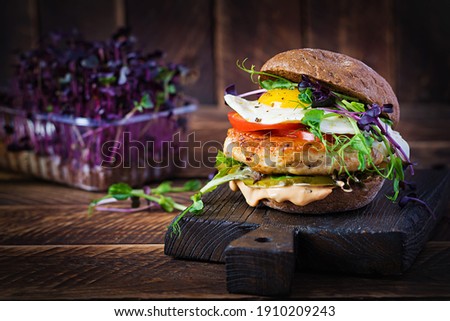 Hamburger. Sandwich with chicken burger, tomatoes,  pickled cucumber and fried egg. Fresh tasty chicken burger on wooden table.