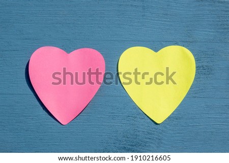 Celebration and special event concept: View from above on one pink and one yellow, empty heart shaped paper stickers on wooden blue background with copy space. For lovers and Valentines day