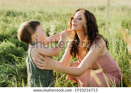 Little boy and mom are holding a dandelion in their hands on the field.