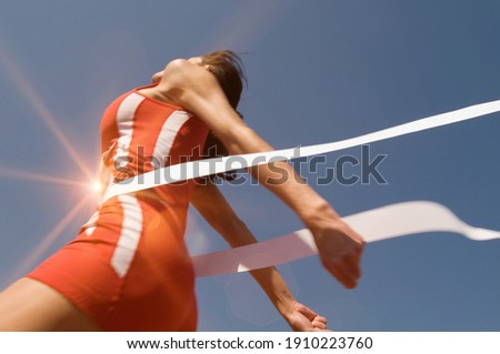 Low angle view of young female athlete crossing finish line against clear blue sky Royalty-Free Stock Photo #1910223760