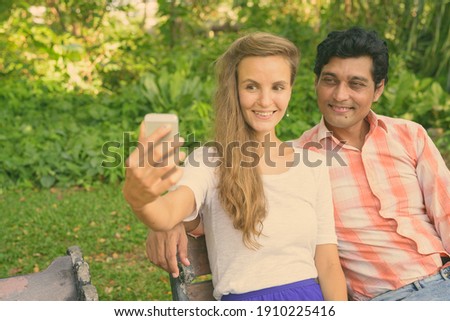 Happy multi ethnic couple taking selfie together and in love at peaceful green park