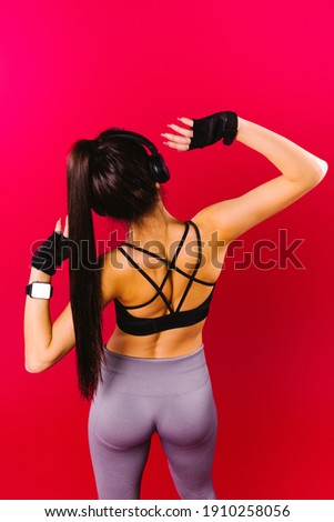 A photo from the back of a girl with inflated buttocks and in a black top with big headphones who is dancing on a red background.