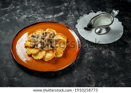 Traditional potato pancakes with forest mushrooms and sour cream on a dark background, raggmunk, draniki, deruny