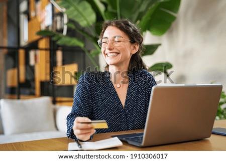 Young happy woman doing shopping online with laptop. Portrait of excited woman holding credit card and buy on an e-commerce site. Beautiful laughing girl paying online bills using debit card. Royalty-Free Stock Photo #1910306017