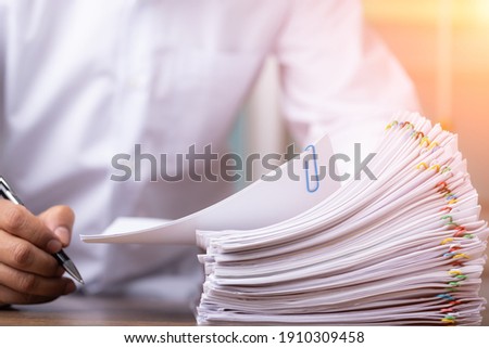 Male office workers holding and writing documents on office desk with light fair, Stack of business overload paper. Royalty-Free Stock Photo #1910309458