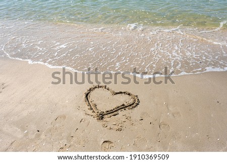 blurred of drawing heart on a yellow sand at a beautiful seascape background. Horizontal composition.