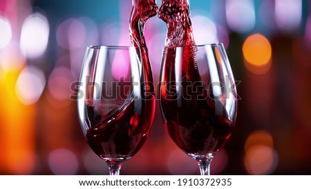 Two glasses of red wine hitting each other, blur bottles with bar counter on background Royalty-Free Stock Photo #1910372935