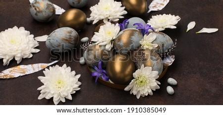 Festive Easter holiday greeting card. Easter Decoration with gray blue golden eggs, quail feathers, white flowers on dark wooden background. Happy Easter card concept. Selective focus, copy space.