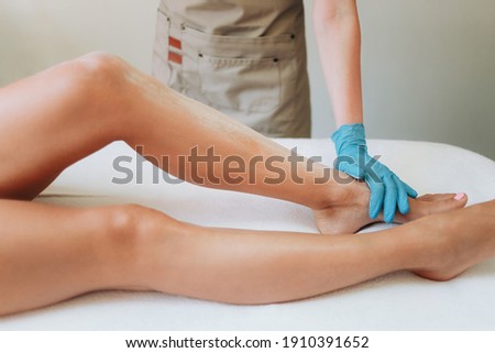Cosmetologist is distributing talcum powder on a young girl's leg before the epilation procedure. The girl is lying on a couch in a beauty salon, she does the procedure shugaring or waxing