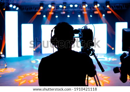 Professional cameraman - covering on event with a video, cameraman silhouette on live studio news, Selective focus Royalty-Free Stock Photo #1910421118