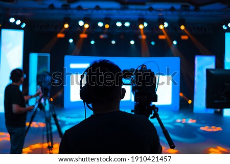 Professional cameraman - covering on event with a video, cameraman silhouette on live studio news, Selective focus Royalty-Free Stock Photo #1910421457