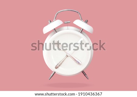 Creative layout of Alarm clock and round plate with cutlery, knife and fork on pink pastel background. Minimal idea business Concept of intermittent fasting, lunchtime, diet and weight loss. Top view 
