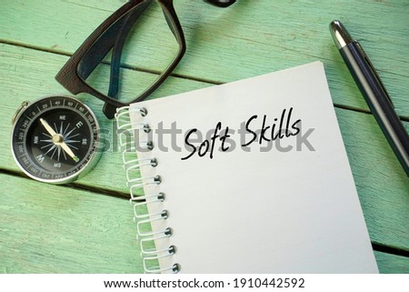 Soft Skills inscription written on open notebook. Compass, spectacle and pen on wooden background.