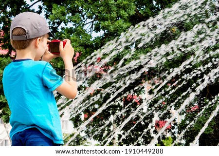 little boy taking pictures of a fountain on a hot summer day