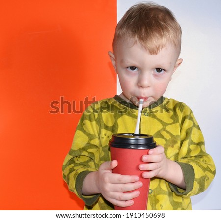 A little boy is drinking from a red glass.