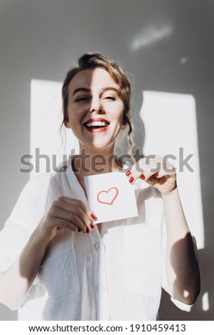 Portrait of a happy young woman on a light background.He holds a drawing of a red heart in his hands.Love, friendship, and a declaration of love.The concept of heart health and organ donation