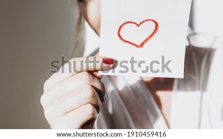 Close-up of a woman's manicured hands holding a drawing of a red heart.Happy Valentine's Day. Love, friendship, and a declaration of love.The concept of heart health and organ donation