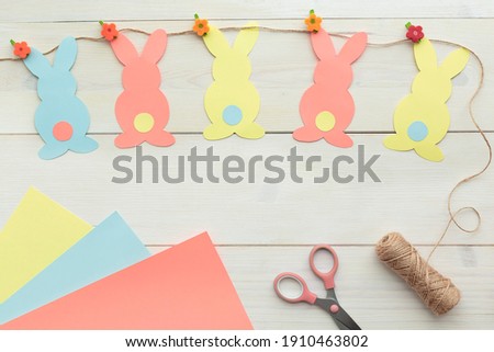 Easter bunny decoration. Paper cut DIY holiday colorful rabbits garland and craft tools.Top view, copy space on wood background.
