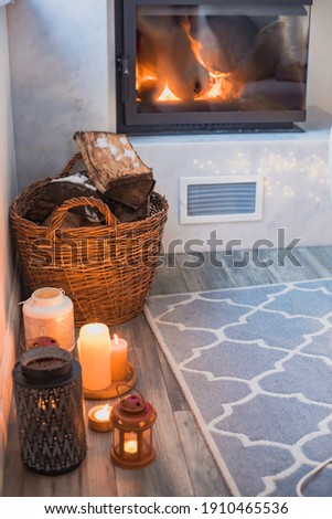 Interior of a cozy room in winter. A room with a fireplace next to which is a basket with firewood. There are different candles on the floor