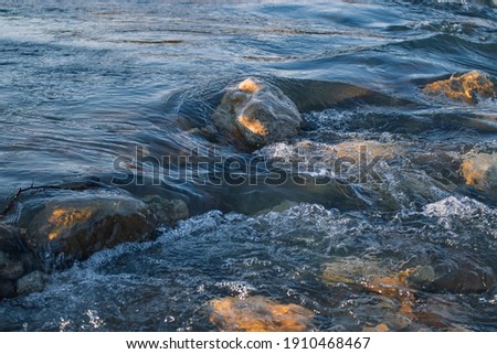 Bubbling water stream of a mountain river with splashes of large stones of a rocky channel on a sunny day.