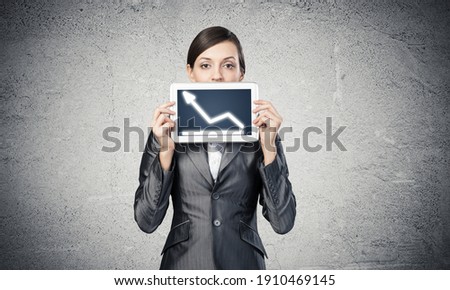 Businesswoman holding tablet computer with growing chart on screen. Beautiful woman in business suit show tablet PC. Corporate businessperson on grey wall background. Digital technology layout.