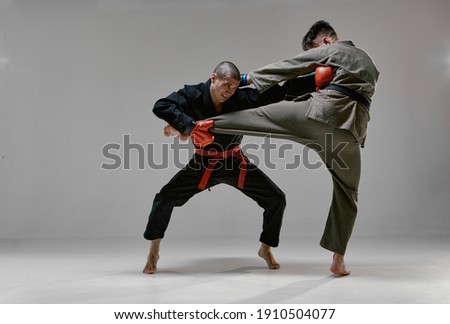 Fighting guys during mixed fight workout. Athletic males in kimono and boxing gloves training martial arts technique 