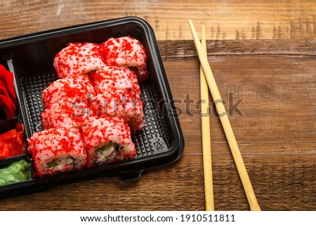 Roll with shrimp, cucumber, wasabi cream cheese and tobiko caviar and sticks in a box with ginger on a wooden background next to sticks. copy space