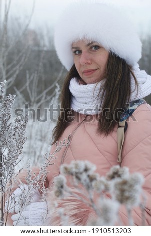 Portrait of a girl for a walk in a winter park. The plants are covered with frost and snow.